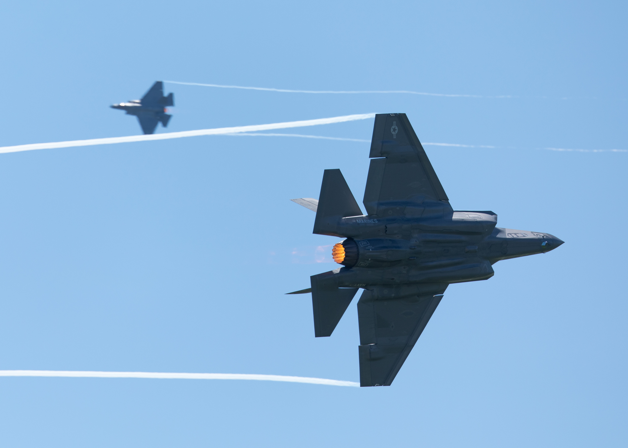 F35 Lightning II in a high G maneuver, with condensation trails forming at the wings tip and afterburners on, during a dogfight with another F-35